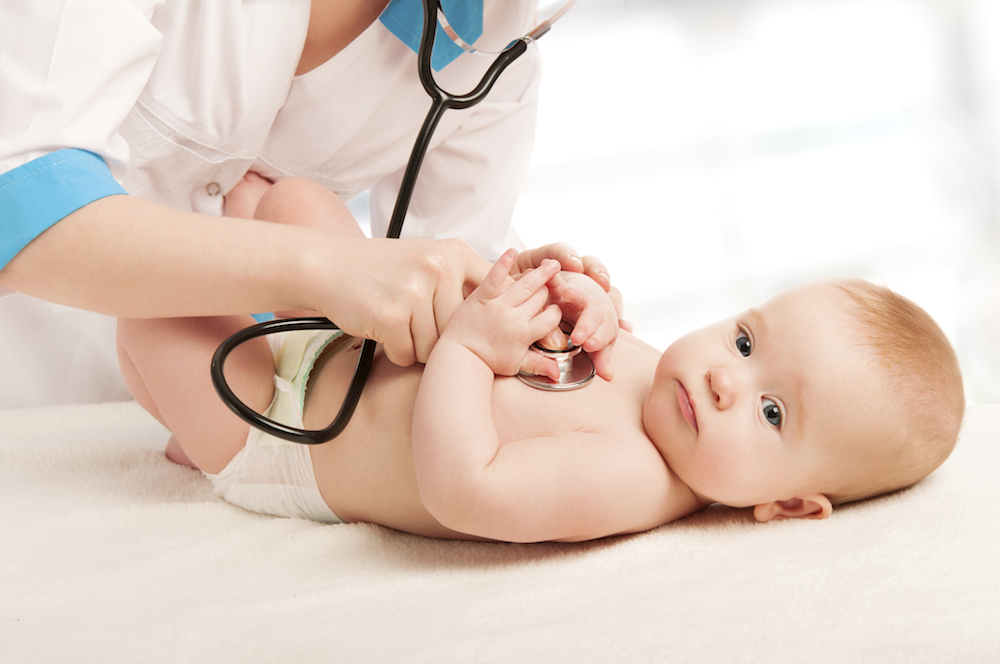 A baby laying down with a doctor placing a stethoscope to its chest